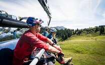 Biker sitzen auf einem Sessellift und geniessen die Aussicht auf grüne Wiesen und Kühe | © Bergbahnen Flumserberg AG