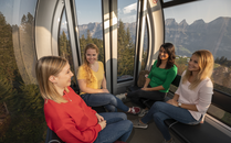 Vier junge Frauen sitzen und unterhalten sich in einer Gondel mit Aussicht auf die Berge | © Bergbahnen Flumserberg AG