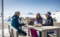 Drei Personen geniessen in Skikleidung ein Fondue auf einer Terrasse einer Berghütte | © Bergbahnen Flumserberg AG