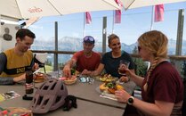 Vier Personen sitzen beim Essen an einem Tisch. Alle in Bike-Kleidung | © Bergbahnen Flumserberg AG
