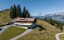 Berghütte mit grosser Sonnenterasse in einer Berglandschaft, im Hintergrund eine Seilbahn | © Bergbahnen Flumserberg AG