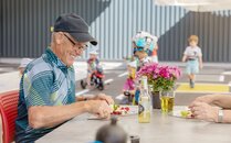 Älterer Mann ist an einem Tisch im Freien, während im Hintergrund Kinder spielen | © Bergbahnen Flumserberg AG