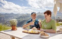 Älteres Paar geniesst eine Käseplatte und stösst mit Weisswein an | © Bergbahnen Flumserberg AG