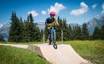Junge sitzt auf einem Bike und fährt über ein Parcourshindernis | © Bergbahnen Flumserberg AG