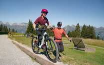 Mädchen fährt auf einem Bike gestützt von einem Mann über einen schmalen Balken | © Bergbahnen Flumserberg AG