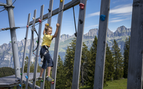 Kleiner Junge klettert in einem Kletterpark vor einer Bergkette | © Bergbahnen Flumserberg AG
