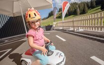 Mädchen mit Helm sitzt auf einem Spielzeugauto | © Bergbahnen Flumserberg AG