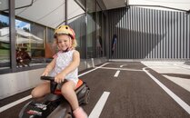 Mädchen mit Helm fährt lachend auf einem Spielzeugauto auf einer Outdoor-Rennstrecke | © Bergbahnen Flumserberg AG