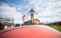 Zwei Kinder springen fröhlich auf einem grossen, roten Luftkissen im Freien | © Bergbahnen Flumserberg AG
