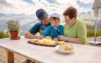 Älteres Paar und ein Kind geniessen ein Käseplättli in einer Bergkulisse | © Bergbahnen Flumserberg AG