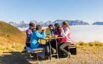 Sechs PErsonen sitzen an einem Holzbank, im Hintergrund Berge und ein Nebelmeer | © Bergbahnen Flumserberg AG