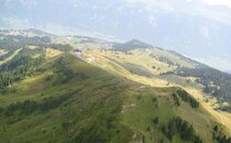 Grüne Wiesen einer Berglandschaft, im Hintergrund eine Bergstation | © Bergbahnen Flumserberg AG