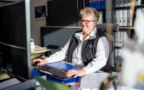 Mitarbeiterin sitzt an einem Schreibtisch und arbeitet am Computer, umgeben von Aktenordnern im Büro | © Bergbahnen Flumserberg AG