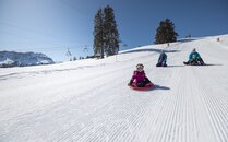 Kleinkind beim Schlitteln auf einer verschneiten Schlittelpiste | © Bergbahnen Flumserberg AG